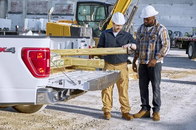 Deux hommes portant des casques de sécurité sur un chantier de construction, retirant du bois de l’arrière d’une camionnette.